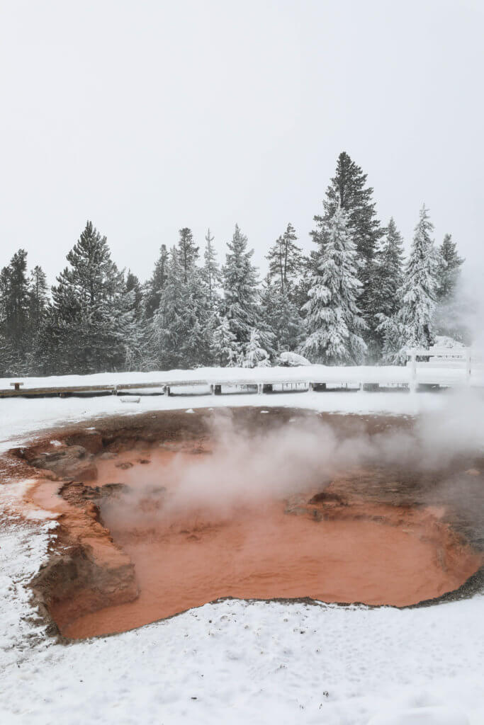 The red water of a paint pot surrounded by snow in Yellowstone. Discover Yellowstone's best kept secret. And for more travel tips and wanderlust inspiration follow The Scenic Suitcase on Pinterest!