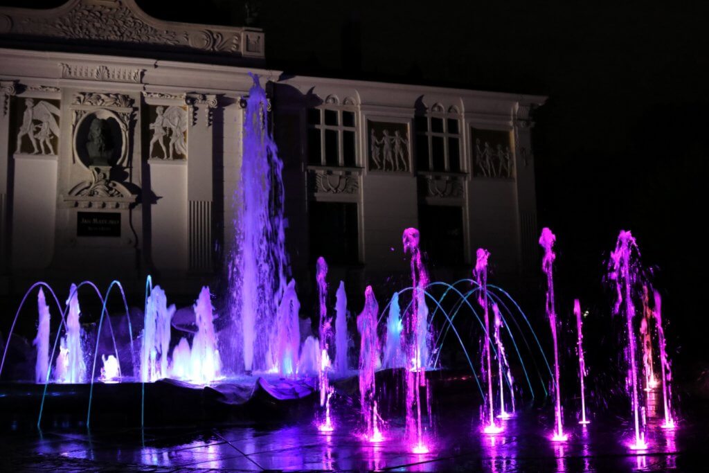 The Glowny Palac Sztuki fountains lit up with multiple dancing colors at night. Just one of the many reasons to visit Krakow, Poland. For more travel tips and wanderlust inspiration follow The Scenic Suitcase on Pinterest!