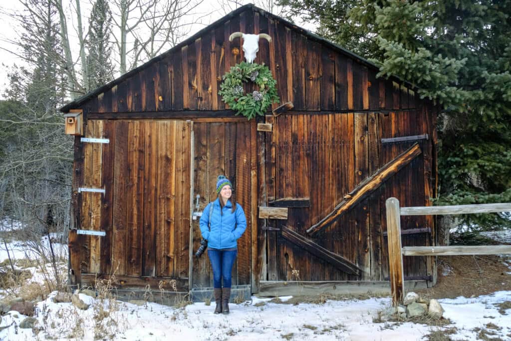 Standing outside a rustic barn with a wreath and cow skull in the snow. Discover 20 picture perfect reasons to visit Colorado in winter. And for more travel tips and wanderlust inspiration follow The Scenic Suitcase on Pinterest!