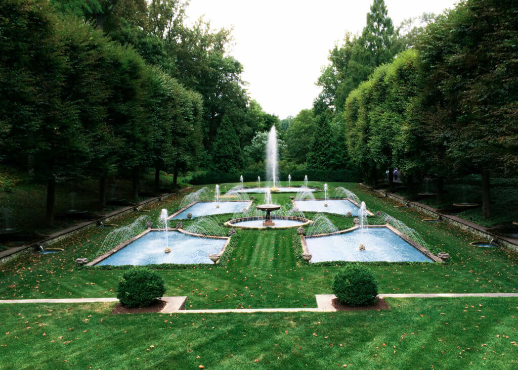 Large fountains in a green space lined with trees. Discover the many reasons why you should visit Longwood Gardens in Kennett Square, Pennsylvania. From beautiful blooms to fantastic fountains, here's what you shouldn't miss. And for more wanderlust inspiration and travel tips, follow The Scenic Suitcase on Pinterest!