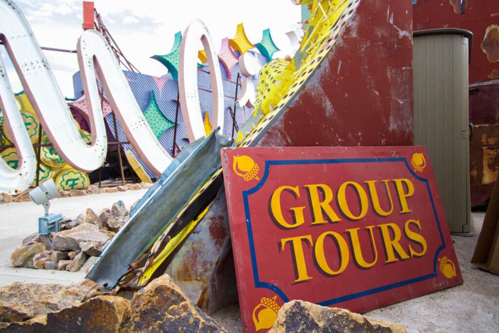 A group tours sign leaning against old neon signs. Visiting the Neon Boneyard is a must when you're in Las Vegas. Discover the rich history behind these Sin City icons, and what you need to know before you go! And for more travel tips and wanderlust inspiration, follow The Scenic Suitcase on Pinterest!