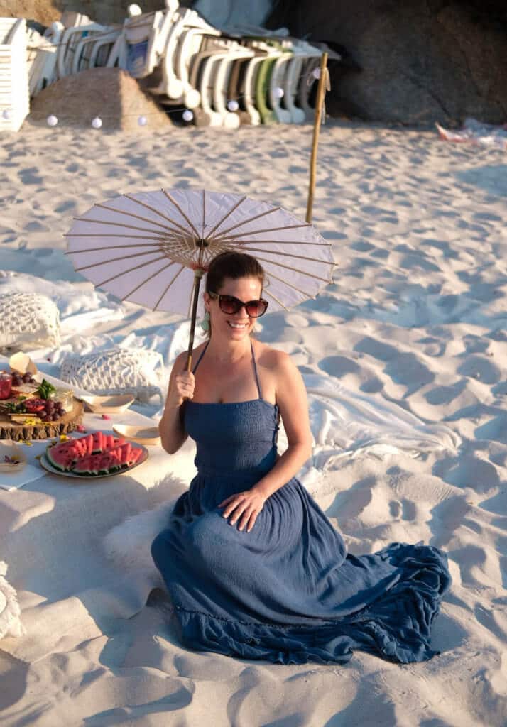 Girl sitting on the beach in a blue dress holding an umbrella. Find out why attending The Blonde Abroad photography tour is a once-in-a-lifetime experience you shouldn't miss. And for more travel tips and wanderlust inspiration, follow The Scenic Suitcase on Pinterest!