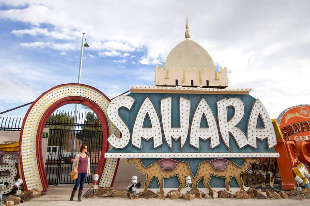 Standing next to the vintage Sahara neon sign. Visiting the Neon Boneyard is a must when you're in Las Vegas. Discover the rich history behind these Sin City icons, and what you need to know before you go! And for more travel tips and wanderlust inspiration, follow The Scenic Suitcase on Pinterest!