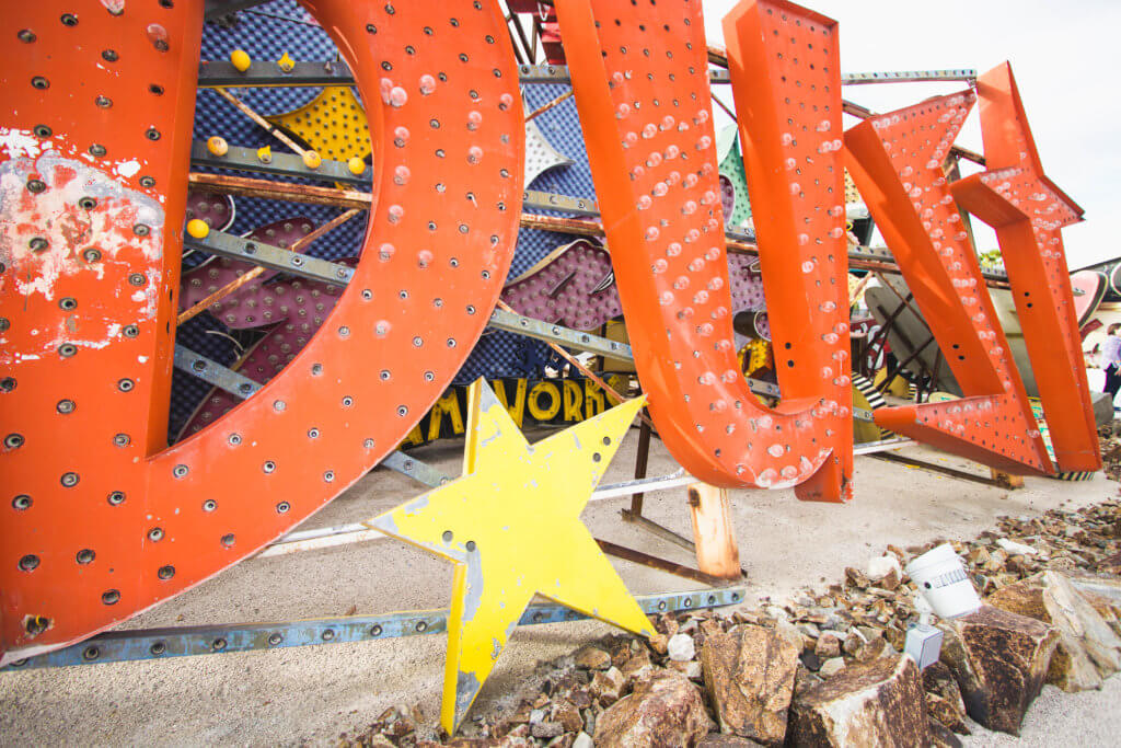 Orange neon letters and a large yellow star sitting amongst rocks. Visiting the Neon Boneyard is a must when you're in Las Vegas. Discover the rich history behind these Sin City icons, and what you need to know before you go! And for more travel tips and wanderlust inspiration, follow The Scenic Suitcase on Pinterest!