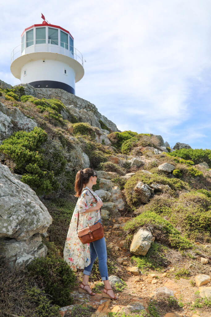 A girl standing on a hill near a lighthouse at Cape of Good Hope. There are a million reasons to visit South Africa. The country is as diverse as it is beautiful and offers countless activities and bucket list adventures. Find out what you can't miss! And for more travel tips and wanderlust inspiration follow The Scenic Suitcase on Pinterest!