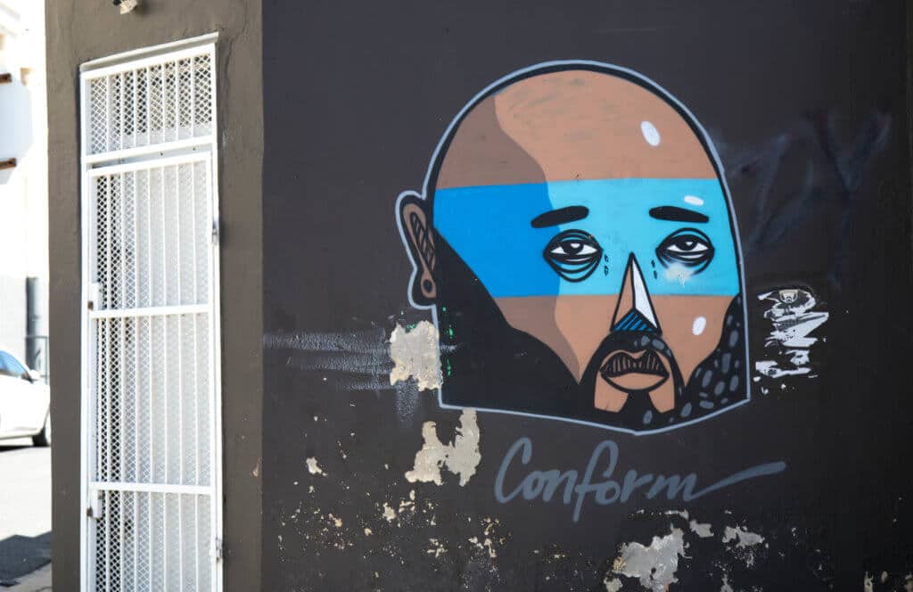 Graffiti of a man with a blue striped face. Discover the unique street art of Woodstock in South Africa. Find out the history behind this eclectic district and why it's a must on any visit to Cape Town! And for more travel tips and wanderlust inspiration follow The Scenic Suitcase on Pinterest!