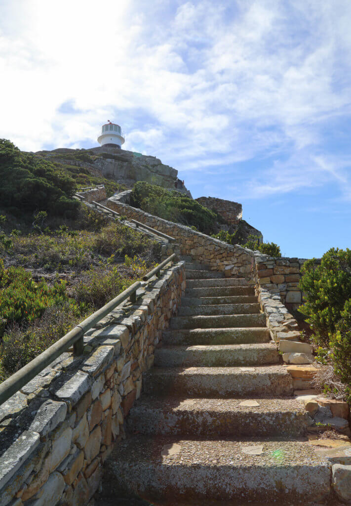 Stairs up to a lighthouse on a hill. There are a million reasons to visit South Africa. The country is as diverse as it is beautiful and offers countless activities and bucket list adventures. Find out what you can't miss! And for more travel tips and wanderlust inspiration follow The Scenic Suitcase on Pinterest!