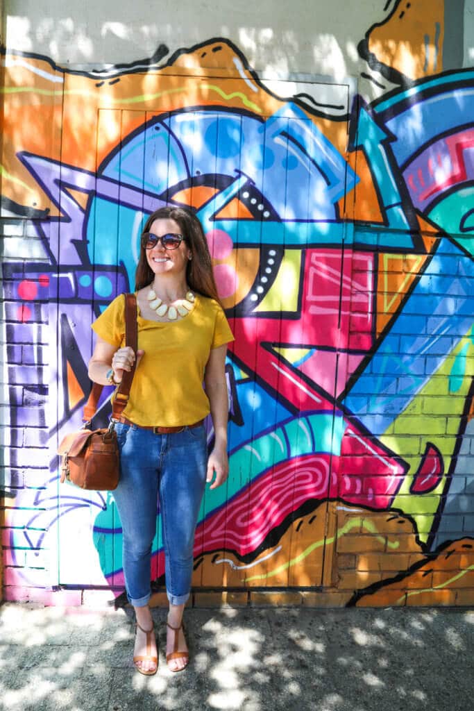 Girl standing in front of colorful graffiti. Discover the unique street art of Woodstock in South Africa. Find out the history behind this eclectic district and why it's a must on any visit to Cape Town! And for more travel tips and wanderlust inspiration follow The Scenic Suitcase on Pinterest!