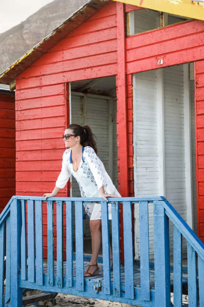 Girl standing on the deck of a red and blue hut. There are a million reasons to visit South Africa. The country is as diverse as it is beautiful and offers countless activities and bucket list adventures. Find out what you can't miss! And for more travel tips and wanderlust inspiration follow The Scenic Suitcase on Pinterest!
