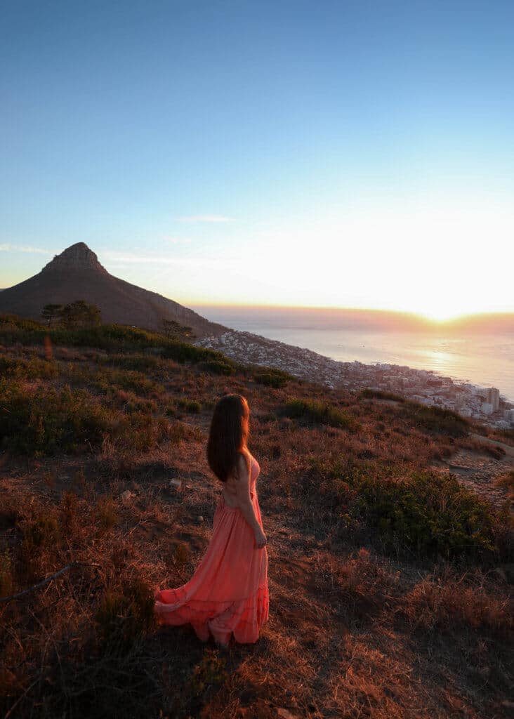 Girl looking out at a sunset over the ocean. There are a million reasons to visit South Africa. The country is as diverse as it is beautiful and offers countless activities and bucket list adventures. Find out what you can't miss! And for more travel tips and wanderlust inspiration follow The Scenic Suitcase on Pinterest!