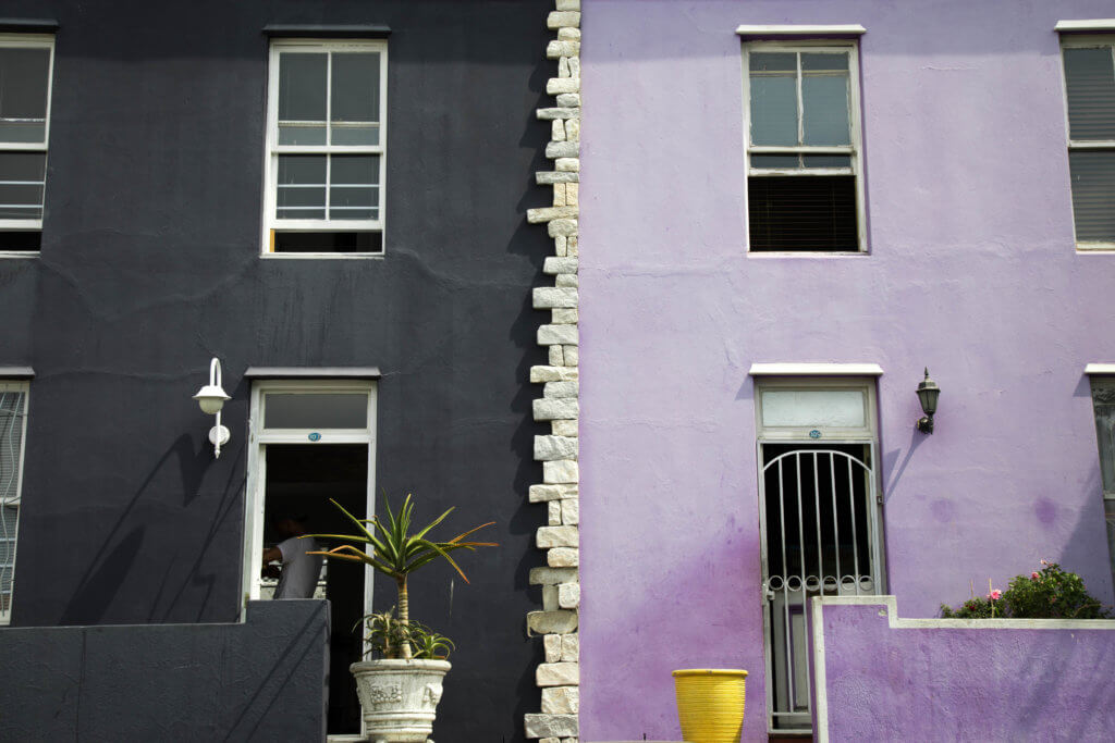 A black and purple building. Visiting Bo Kaap in Cape Town feels like stepping into a cartoon. But there's more to the neighborhood than prismatic facades. Discover the colorful history of one of South Africa's most intriguing communities. Plus, get expert tips on what you need to know before you go! And for more travel tips, follow The Scenic Suitcase on Pinterest!