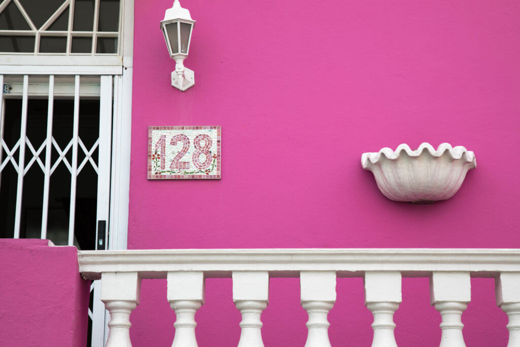A birght pink building facade. Visiting Bo Kaap in Cape Town feels like stepping into a cartoon. But there's more to the neighborhood than prismatic facades. Discover the colorful history of one of South Africa's most intriguing communities. Plus, get expert tips on what you need to know before you go! And for more travel tips, follow The Scenic Suitcase on Pinterest!