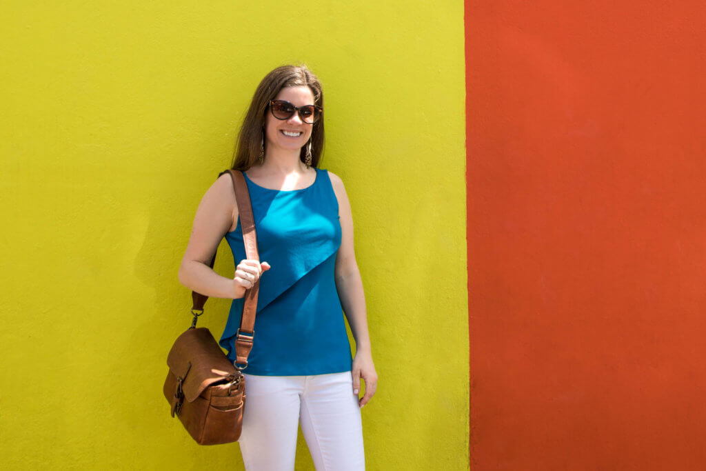 A girl in blue and white standing next to a yellow and orange building. Visiting Bo Kaap in Cape Town feels like stepping into a cartoon. But there's more to the neighborhood than prismatic facades. Discover the colorful history of one of South Africa's most intriguing communities. Plus, get expert tips on what you need to know before you go! And for more travel tips, follow The Scenic Suitcase on Pinterest!