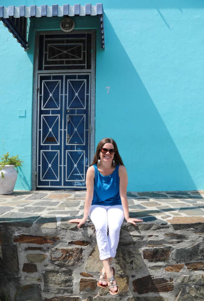 A girl in white and blue sitting on the stone ledge of a blue building. Visiting Bo Kaap in Cape Town feels like stepping into a cartoon. But there's more to the neighborhood than prismatic facades. Discover the colorful history of one of South Africa's most intriguing communities. Plus, get expert tips on what you need to know before you go! And for more travel tips, follow The Scenic Suitcase on Pinterest!