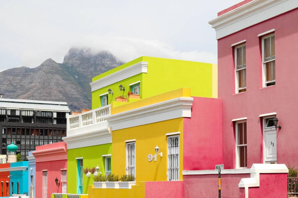 Rainbow exteriors with Table Mountain in the background. Visiting Bo Kaap in Cape Town feels like stepping into a cartoon. But there's more to the neighborhood than prismatic facades. Discover the colorful history of one of South Africa's most intriguing communities. Plus, get expert tips on what you need to know before you go! And for more travel tips, follow The Scenic Suitcase on Pinterest!