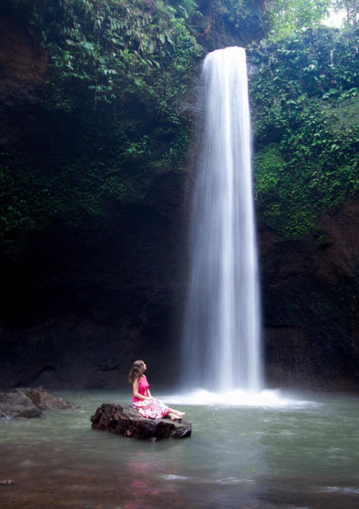 A girl sitting on a rock near a waterfall. Trying to figure out how to use a DSLR camera can feel as impossible as trying to figure out how to launch the space shuttle. But it doesn't have to be complicated! Learn the basics of how to stop shooting in auto and start shooting in awesome! And for more travel and photography tips, follow The Scenic Suitcase on Pinterest!