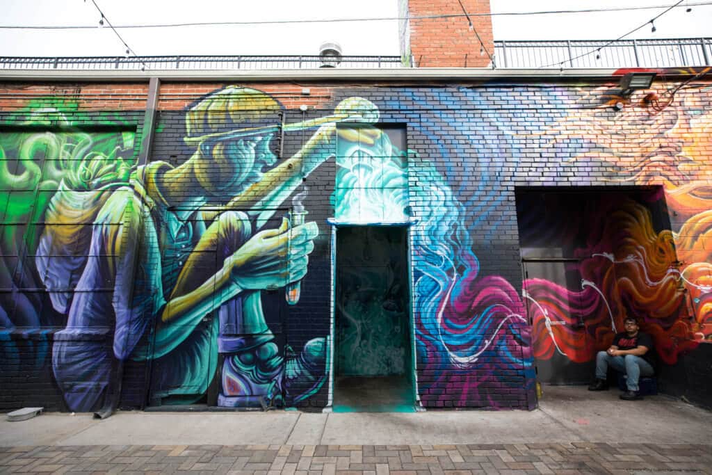 Colorful street art on the side of a building with a man sitting in the doorway. Discover where to find the best street art in Denver! From memorable murals to colorful characters, here's what you need to know. And for more travel tips and wanderlust inspiration, follow The Scenic Suitcase on Pinterest!