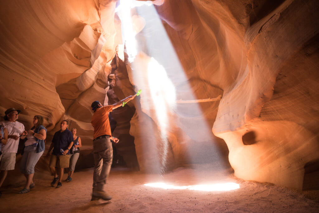 A tour guide shoveling sand into the air in Antelope Canyon. Discover the very best way to photograph Antelope Canyon. From what tour to book, to the camera settings needed for perfect pictures. And for more travel tips and wanderlust inspiration, follow The Scenic Suitcase on Pinterest!