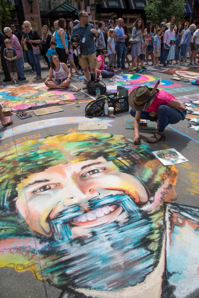 A girl drawing a colorful portrait of Bob Ross with chalk. Find out everything you need to know about the annual Denver Chalk Art Festival! What it's all about, what you can expect, and what you can't miss! And for more travel tips and wanderlust inspiration, follow The Scenic Suitcase on Pinterest!