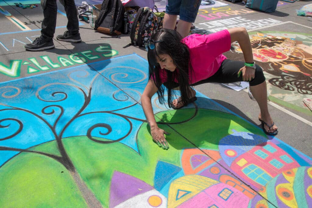 A woman blenidng green chalk in a colorful landscape drawing. Find out everything you need to know about the annual Denver Chalk Art Festival! What it's all about, what you can expect, and what you can't miss! And for more travel tips and wanderlust inspiration, follow The Scenic Suitcase on Pinterest!