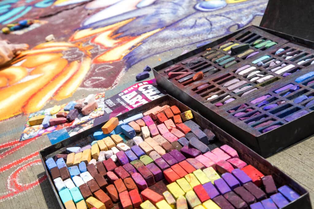 Many different colors of chalk on a tray with a chalk drawing in the background. Find out everything you need to know about the annual Denver Chalk Art Festival! What it's all about, what you can expect, and what you can't miss! And for more travel tips and wanderlust inspiration, follow The Scenic Suitcase on Pinterest!
