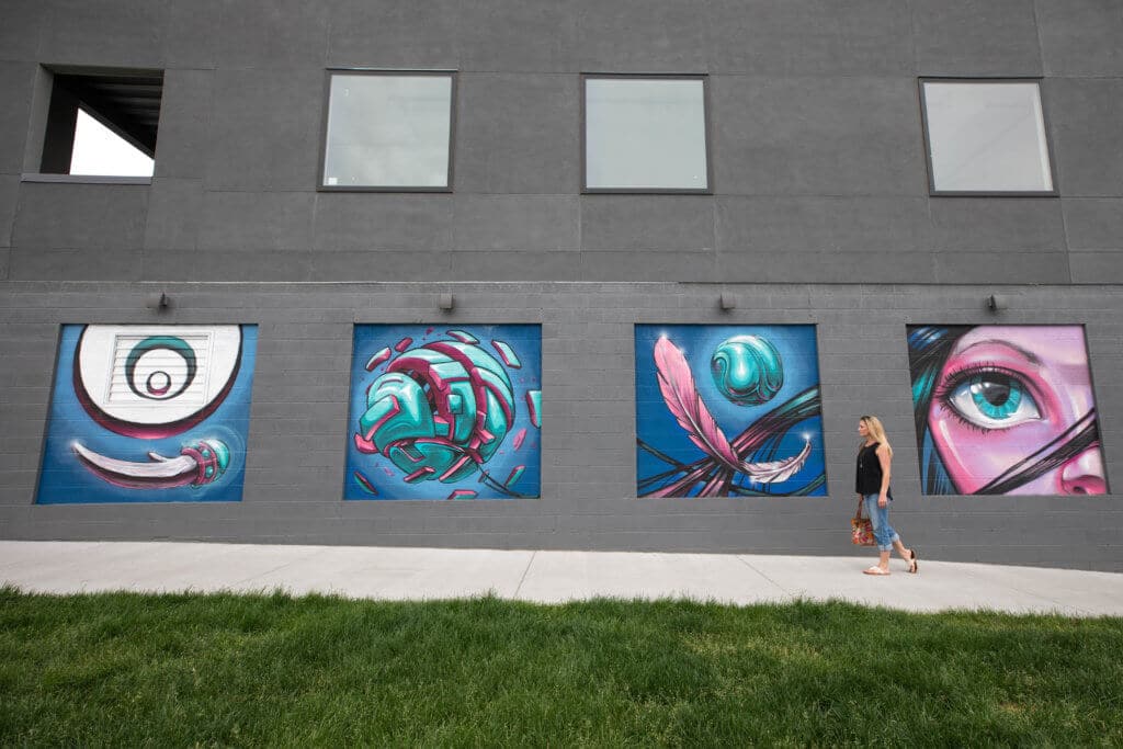 A girl walking past four squares of colorful graffiti art on a grey wall. Discover where to find the best street art in Denver! From memorable murals to colorful characters, here's what you need to know. And for more travel tips and wanderlust inspiration, follow The Scenic Suitcase on Pinterest!