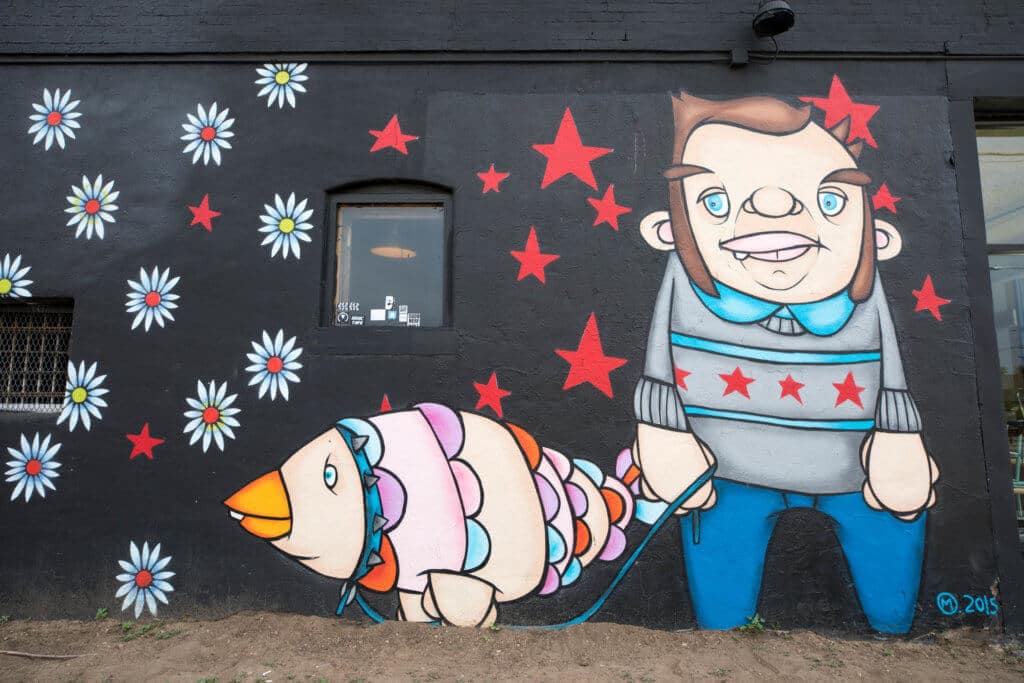 Graffiti art of a man walking a fish with flowers and stars around it. Discover where to find the best street art in Denver! From memorable murals to colorful characters, here's what you need to know. And for more travel tips and wanderlust inspiration, follow The Scenic Suitcase on Pinterest!