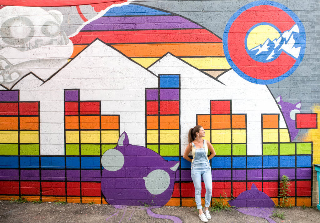 A girl standing along a wall of colorful street art. 