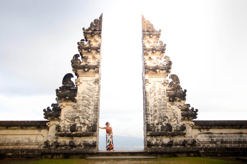 Girl wearing a sarong at intricately carved temple gates at sunrise. Learn 10 travel safety tips every jetsetter should know. How to avoid scams, ways to stay safe abroad, how to ensure your home stays safe, and more! And for additional travel tips and wanderlust inspiration, follow The Scenic Suitcase on Pinterest!