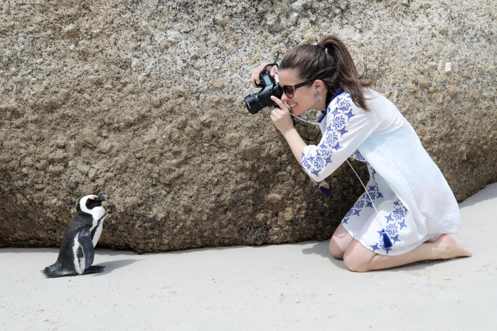 Girl in a white and blue swim cover-up taking a picture sitting next to a penguin. Discover 10 reasons to travel solo, and why seeing the world on your own will rock your socks off. Surprising perks, life-changing opportunities, and more! And for additional travel tips and wanderlust inspiration, follow The Scenic Suitcase on Pinterest!