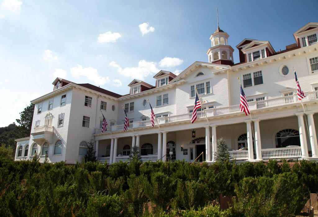 The white exterior of the Stanley Hotel in Estes Park. Discover the most stunning, offbeat, and unique places in Colorado. Including cliff diving dinner entertainment, haunted hotels, towering dunes, and more! And for additional travel tips and wanderlust inspiration, follow The Scenic Suitcase on Pinterest!