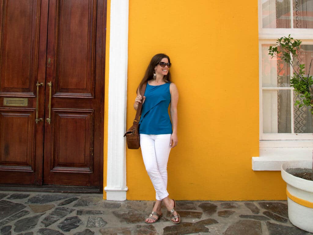 A girl standing against a yellow wall wearing a blue shirt, white pants, and holding a brown leather purse. Learn 10 travel safety tips every jetsetter should know. How to avoid scams, ways to stay safe abroad, how to ensure your home stays safe, and more! And for additional travel tips and wanderlust inspiration, follow The Scenic Suitcase on Pinterest!