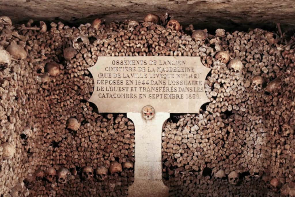Human bones surrounding a plaque sign. Learn the best tips for visiting the Paris catacombs. How to avoid insanely long lines, and what to expect when you get there! And for more travel tips and wanderlust inspiration follow The Scenic Suitcase on Pinterest!