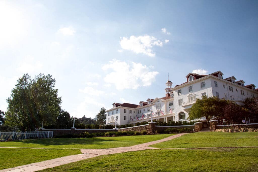 A white hotel on top of a grassy hill. The Stanley Hotel has classic charm, an intriguing past, and otherwordly guests. Discover what it's like to meet ghosts on a Stanley Hotel haunted tour! And for more travel tips and wanderlust inspiration, follow The Scenic Suitcase on Pinterest!