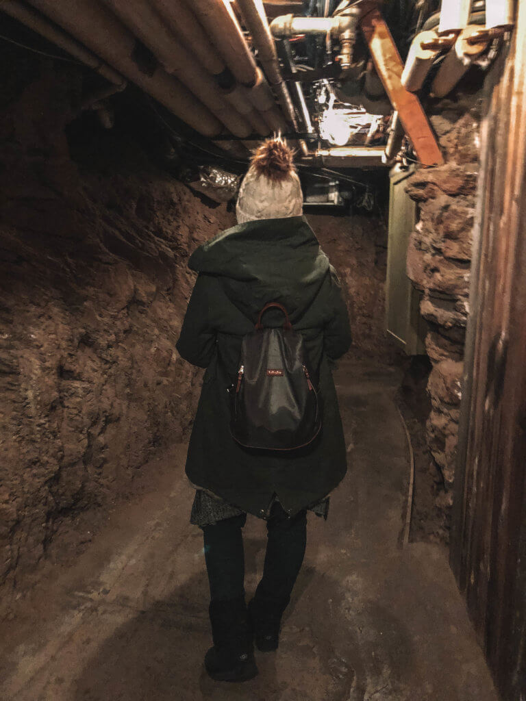 A girl in a white beanie walking down a dark, underground hallway. The Stanley Hotel has classic charm, an intriguing past, and otherwordly guests. Discover what it's like to meet ghosts on a Stanley Hotel haunted tour! And for more travel tips and wanderlust inspiration, follow The Scenic Suitcase on Pinterest!