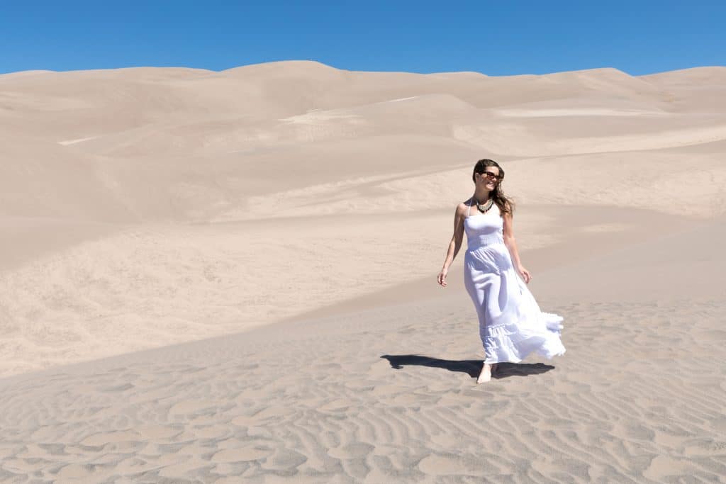 A girl in a white dress walking through the sand dunes. See the most picture perfect moments of 2018. From London to Cape Town to Las Vegas and more, see what you can't miss in these incredible destinations! And for more travel tips and wanderlust inspiration, follow The Scenic Suitcase on Pinterest!