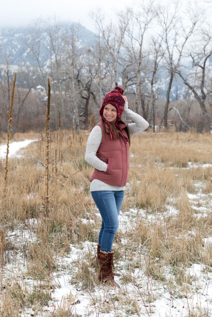 Girl in a pink hat and down vest touching her head while walking through a snowy mountain field. The ultimate winter packing guide with a complete list of items you need for winter travel. Everything you need to stay warm and toasty! And for more travel tips and wanderlust inspiration, follow The Scenic Suitcase on Pinterest!