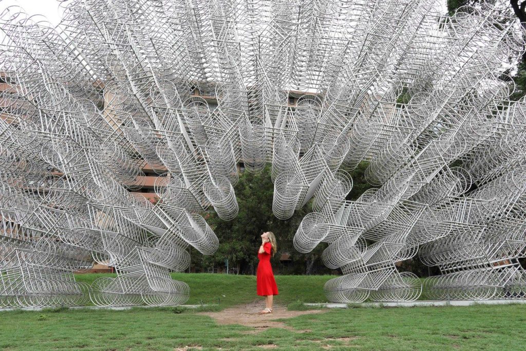 A girl in red looking up at a sculpture made of thousands of silver bikes. See the most picture perfect moments of 2018. From London to Cape Town to Las Vegas and more, see what you can't miss in these incredible destinations! And for more travel tips and wanderlust inspiration, follow The Scenic Suitcase on Pinterest!