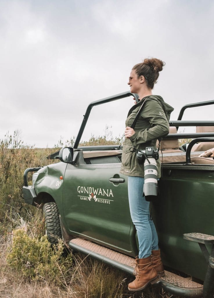 A girl standing on the edge of a safari vehicle holding her camera. Learn what you need to bring on your next African adventure with this essential safari packing guide. And for more travel tips follow The Scenic Suitcase on Pinterest!