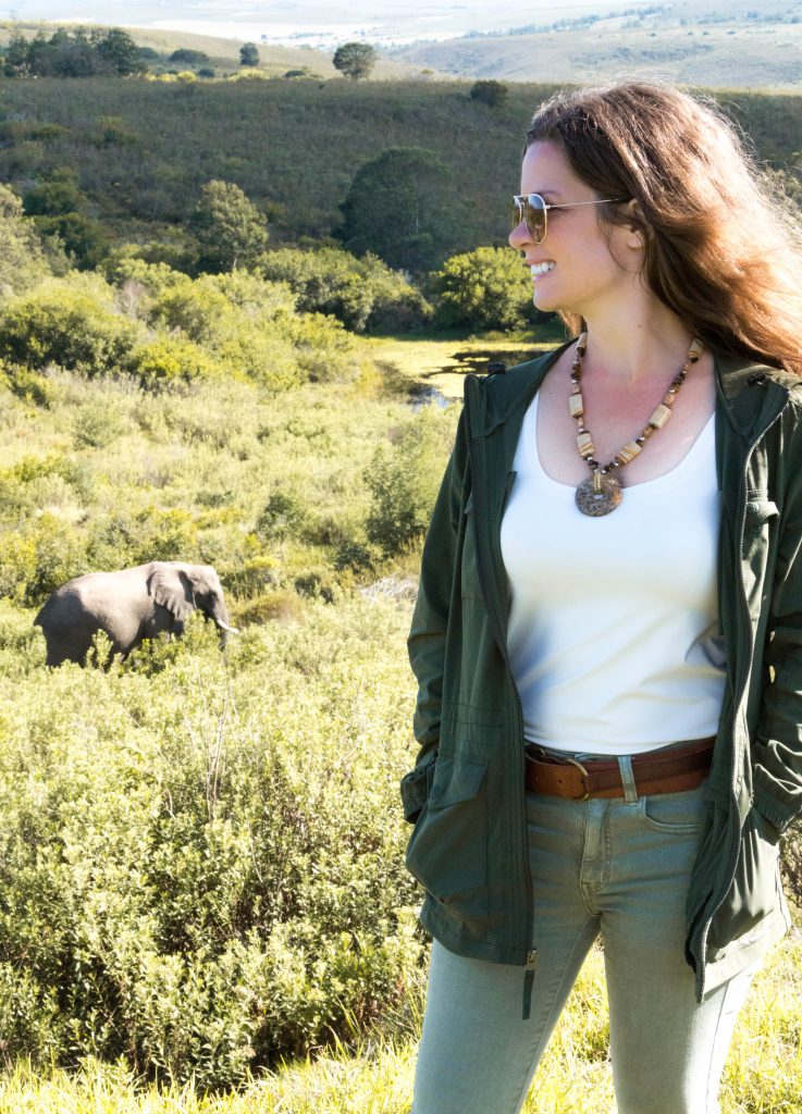 A girl standing on a hillside smiling as an elephant walks by in the distance. Learn what you need to bring on your next African adventure with this essential safari packing guide. And for more travel tips follow The Scenic Suitcase on Pinterest!