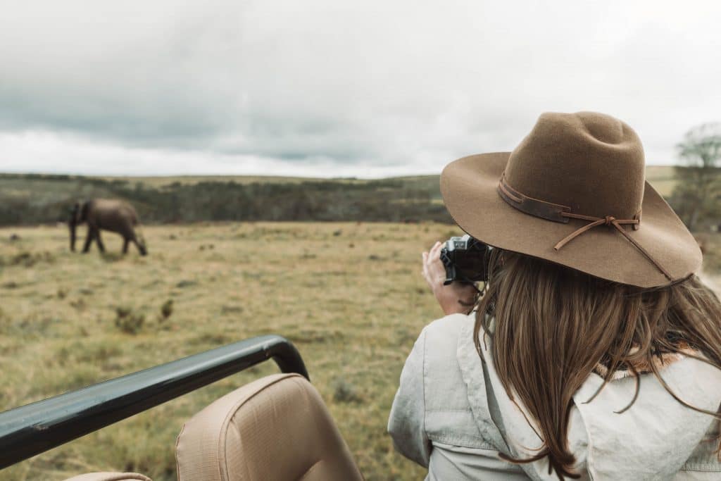 A girl in a brimmed hat photographing an elephant walking by in the distance. Learn what you need to bring on your next African adventure with this essential safari packing guide. And for more travel tips follow The Scenic Suitcase on Pinterest!