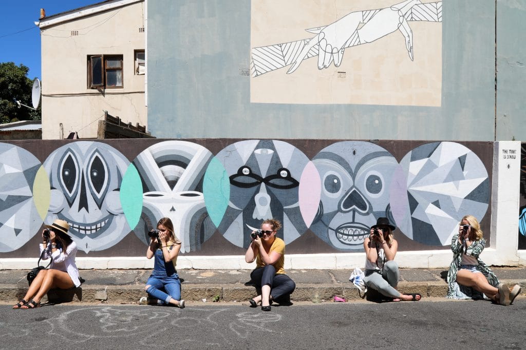 Girls sitting on a curb in a row holding up cameras. Discover 10 photography ideas to boost your creativity! Get out of the slump and get shooting! And for more tips, follow The Scenic Suitcase on Pinterest! #photographytips #photographyinspiration