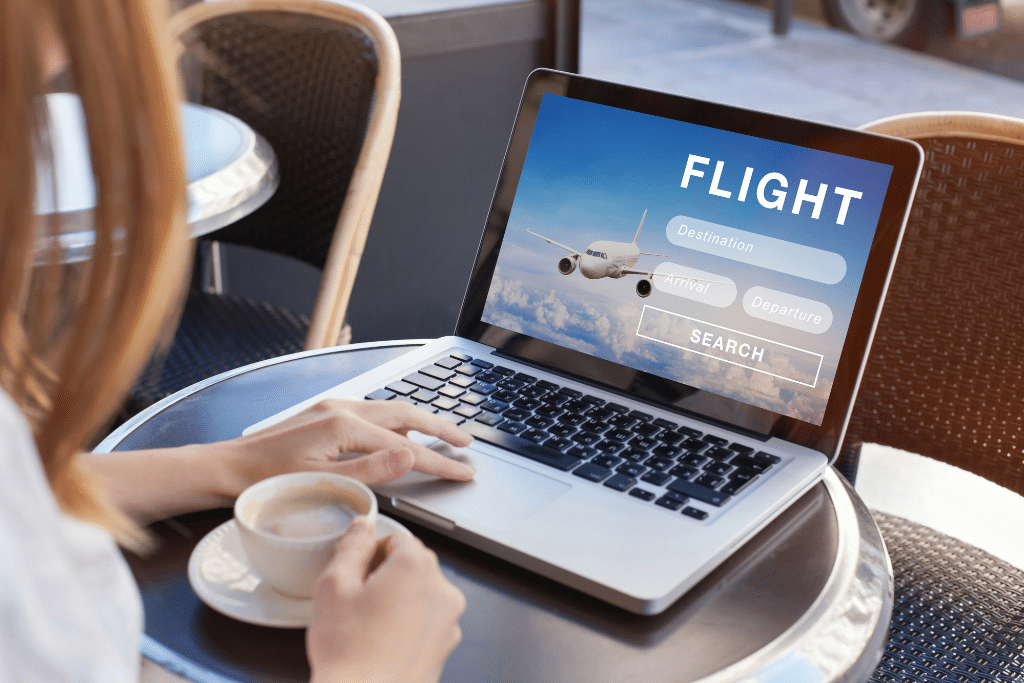 Someone drinking coffee while booking a flight on their laptop.