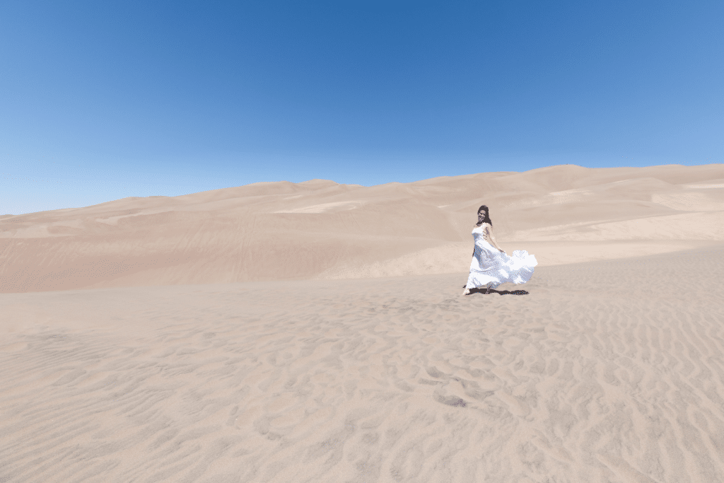 Girl in a white dress walking through sand dunes.