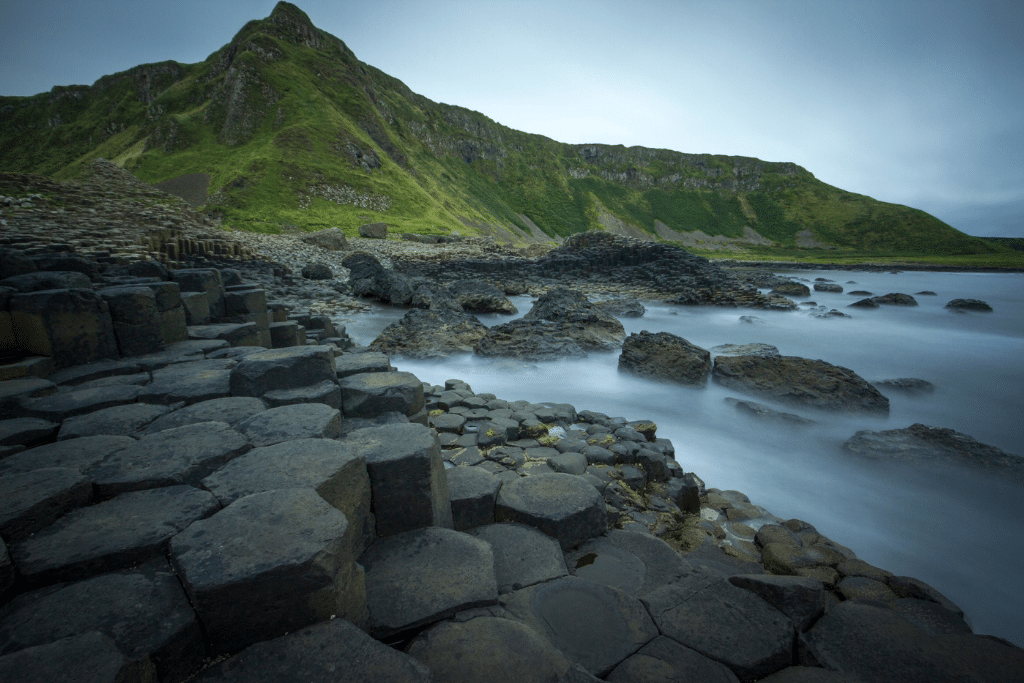 A gloomy day on the shore of Giant's Causeway with a green mountain in the background.