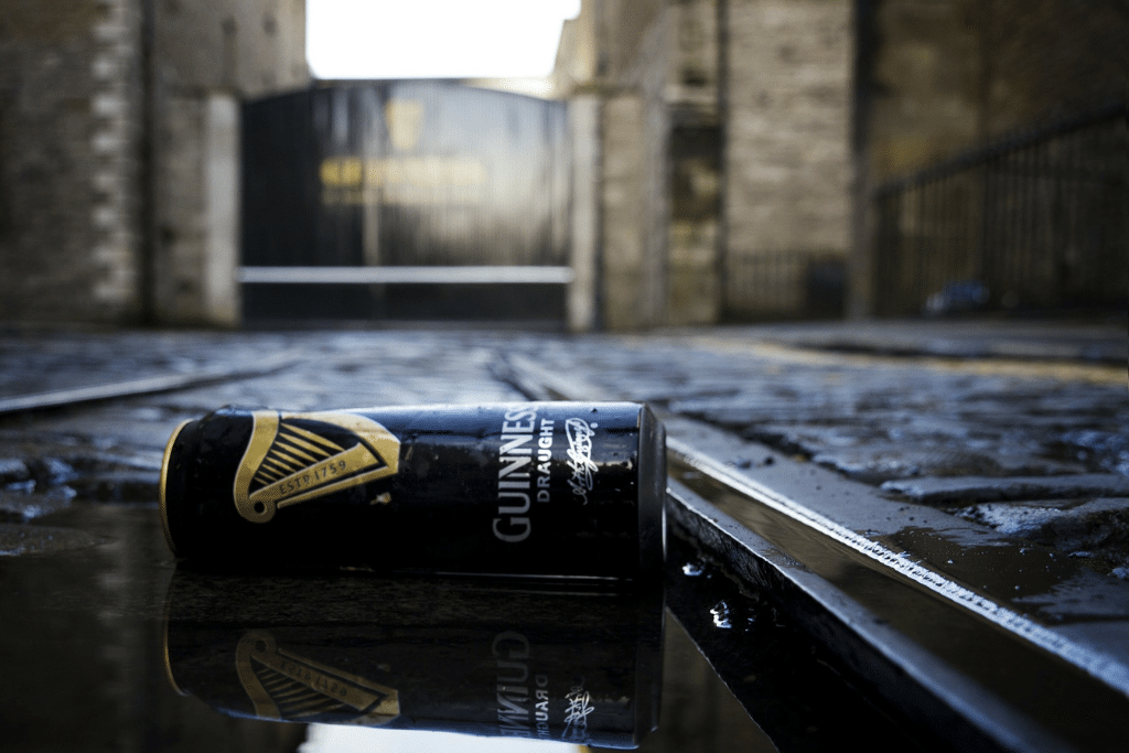 An empty Guinness beer can laying in a puddle on the street. #GuinnessStorehouse