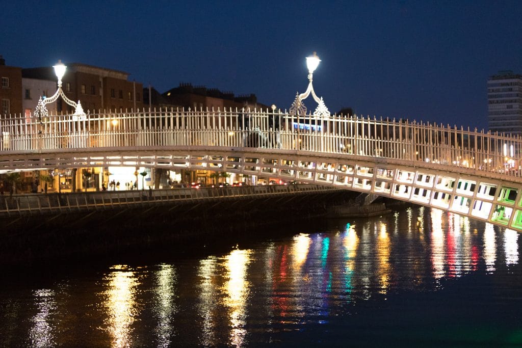 The white Ha'Penny Bridge at night with lights on the Liffey River. #HaPennyBridge
