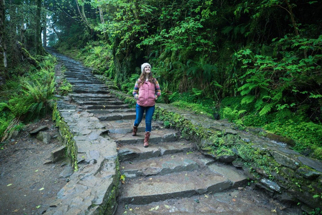 A girl walking down stone steps in a green forest. It's one of the most amazing things to see in Killarney! #TorcWaterfall #Killarney