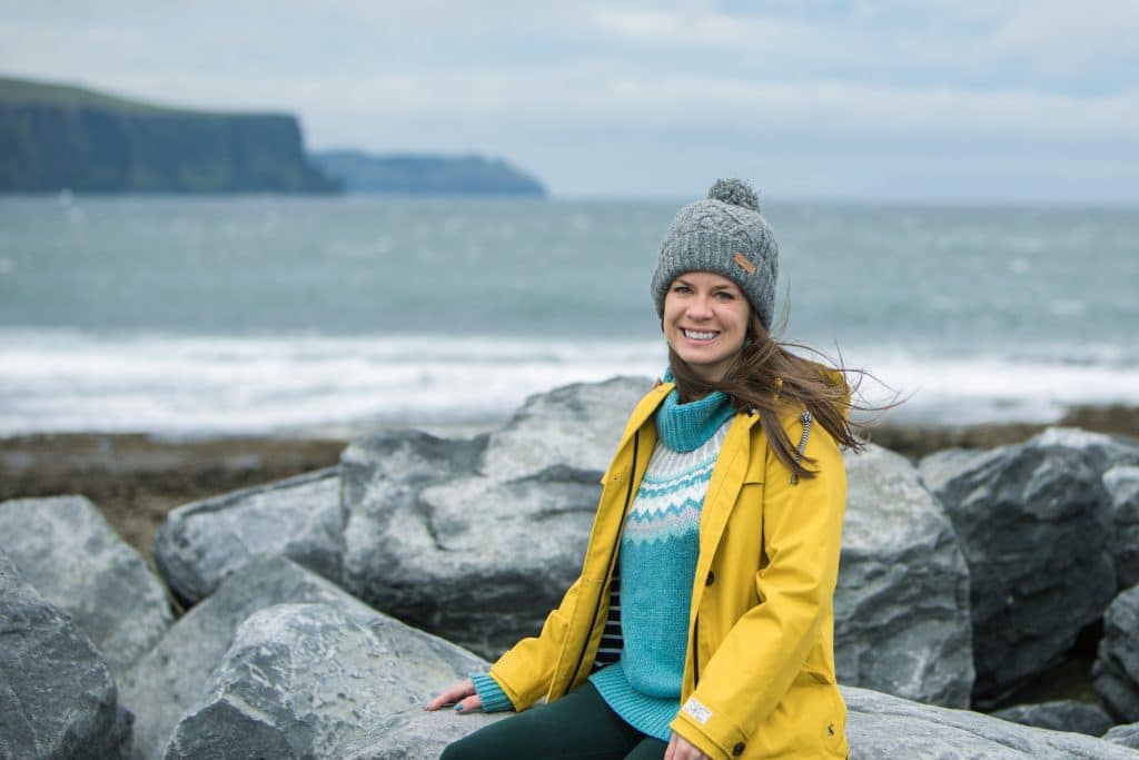 Girl sitting along the shore with the Cliffs of Moher in the background.