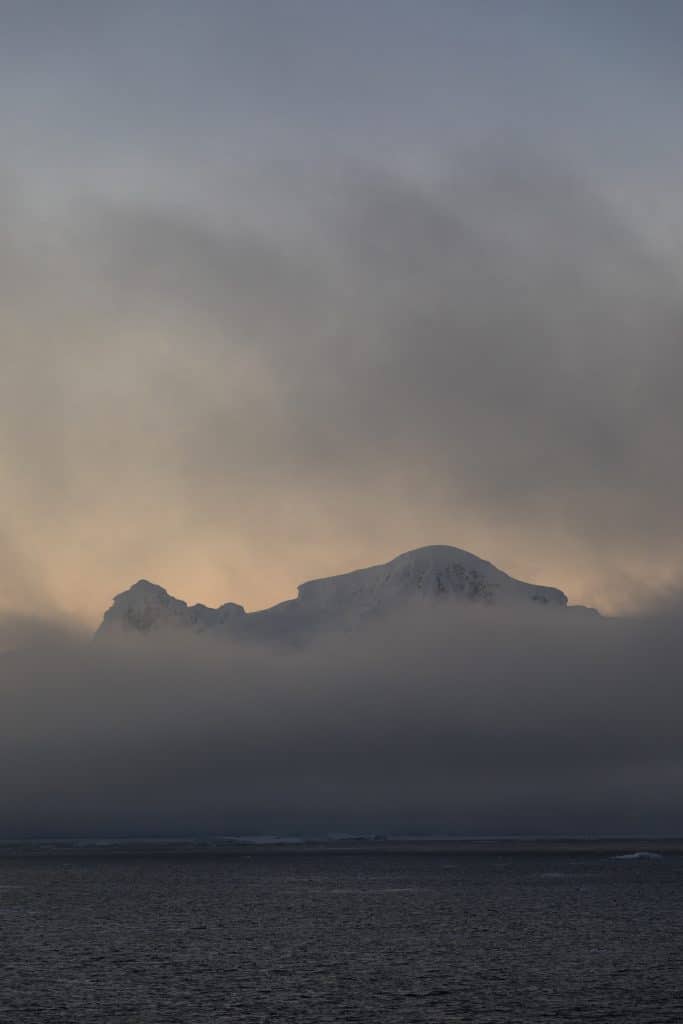 Mountains peaking through the clouds at sunset in Antarctica. #antarctica